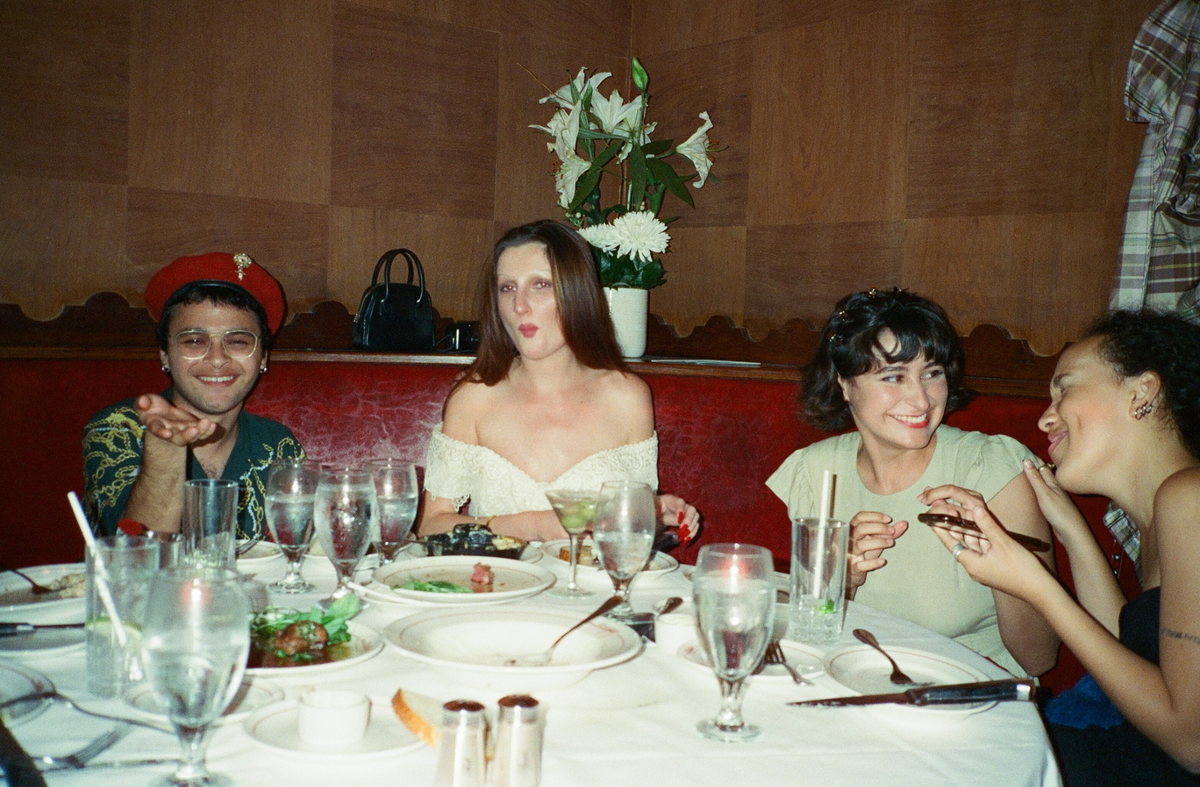 Friends gathered at a red booth with a round table, laughing and eating.